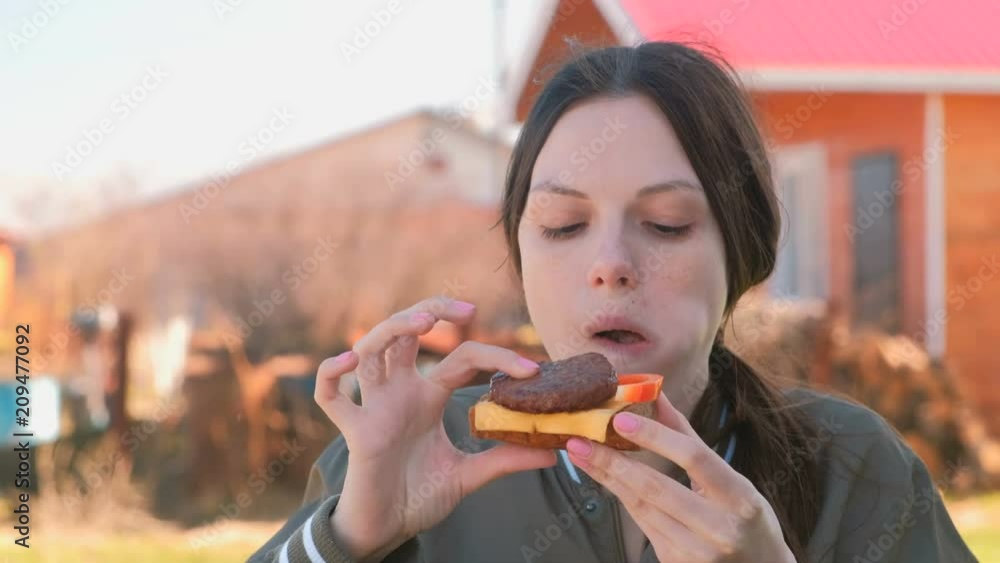 Young woman with blue braid hairs eats sandwich with bread, cutlet, pepper and cheese outdoor. Young woman with blue braid hairs eats sandwich with bread, cutlet, pepper and cheese outdoor.
