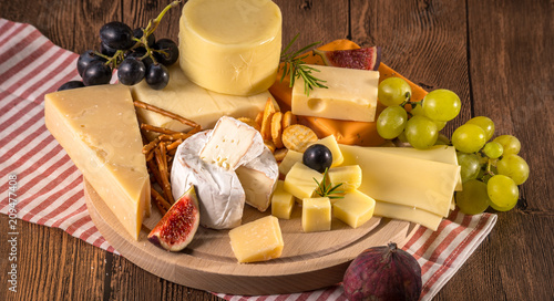 Assorted cheeses on round wooden board plate Camembert cheese, cheese grated bark of oak, hard cheese slices, walnuts, grapes, crackers, bread, thyme, wood background.