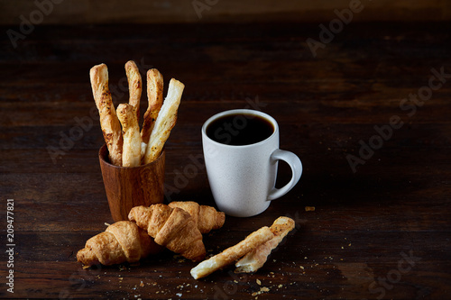 Coffee cup, breadsticks and croissants on an old wooden background, close-up, selective focus.