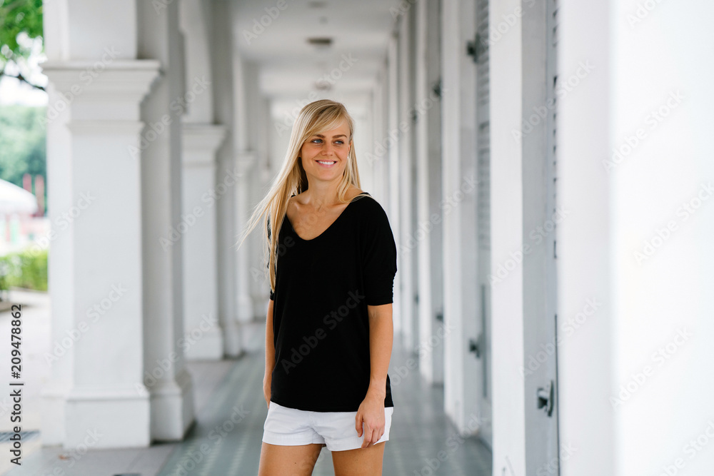Portrait of a young and beautiful blonde exchange student standing in the corridor of her campus. She is wearing comfortable clothes and smiling as she looks around the place.