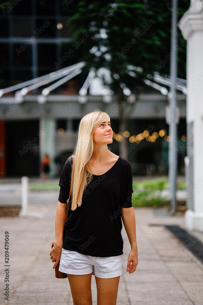 Fototapeta premium An image of a pretty blonde girl walking outside of an old colonial building on a sunny day. She is wearing a comfortable clothes and she enjoys looking around the place.