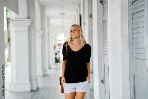 Portrait of a young and attractive blonde woman with blue eyes roaming around a colonial house. She is casually and comfortably dressed. She enjoys taking a tour of her new campus.