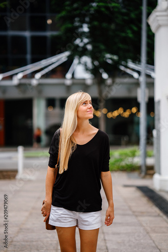 An image of a pretty blonde girl walking outside of an old colonial building on a sunny day.  She is wearing a comfortable clothes and she enjoys looking around the place. © Danon