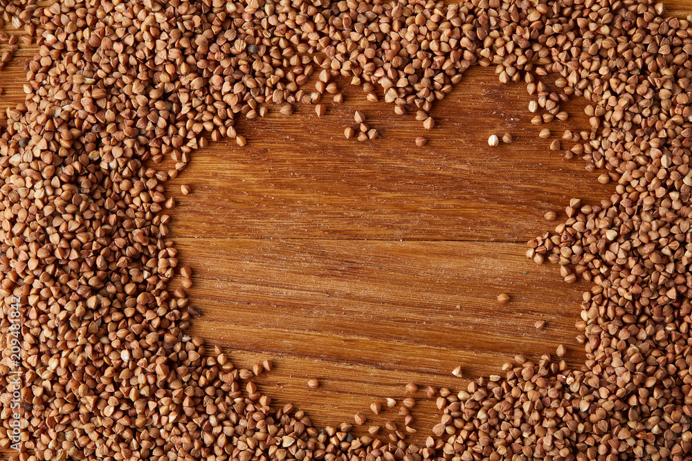 Buckwheat groats arranged in a frame on wooden background, top view, close-up, selective focus. Buckwheat groats arranged in a frame on wooden background, top view, close-up, selective focus.