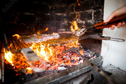 Big pork steak on the glowing charcoal grill, huge fire, burning pork meat