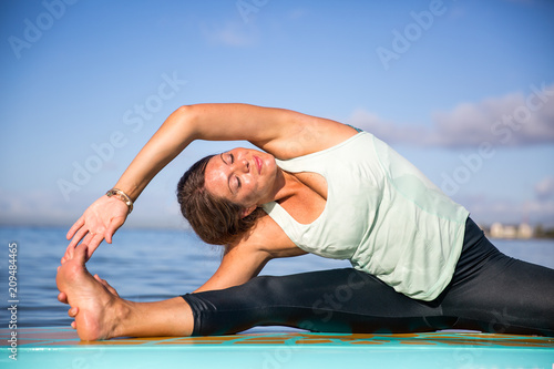 Athletic young woman in SUP Yoga practice side bend Pose in Ala Moana Hawaii