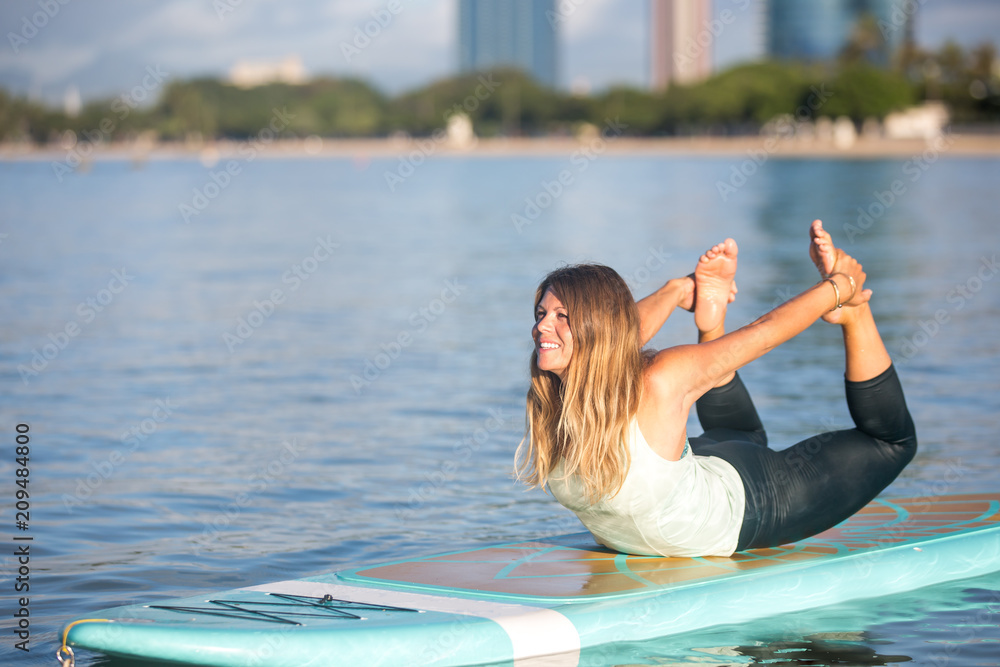 Pretty woman in bow pose doing SUP Yoga on the water