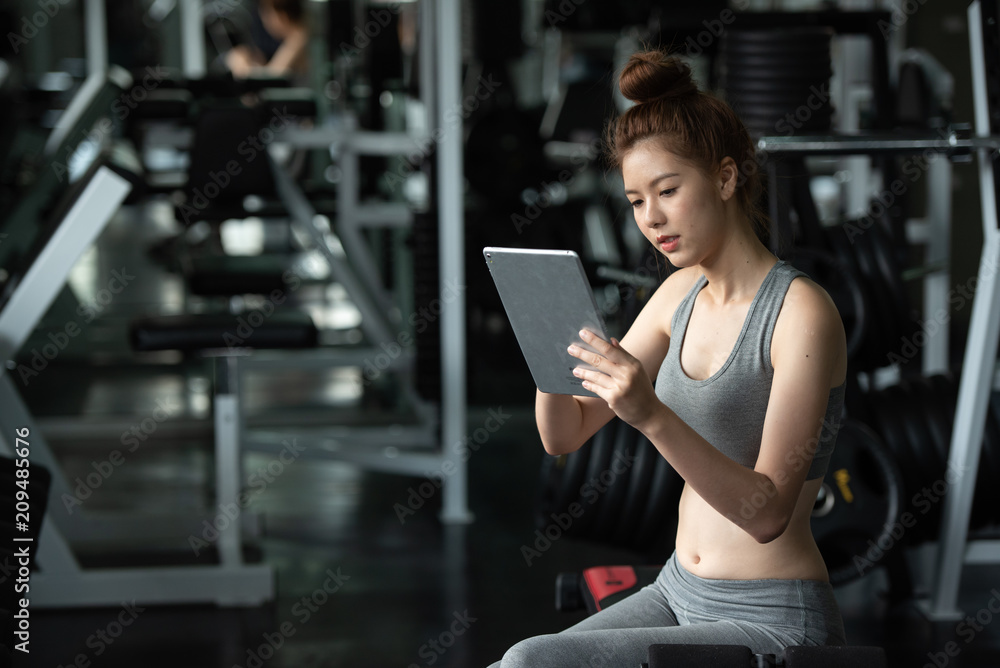 Young sport woman relaxing by using tablet in the gym after exercise. Young sport woman relaxing by using tablet in the gym after exercise.
