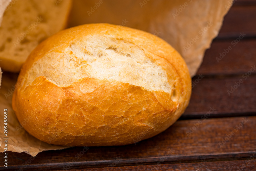 Fresh baked bread wrapped in paper, on wooden background