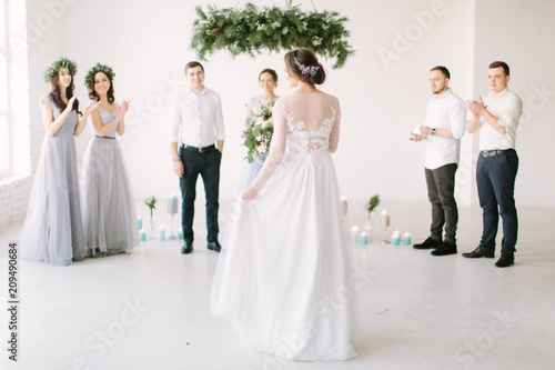 Fotografie Beautiful bride in a white dress holds a wedding bouquet and is going to her groom with bridesmaids and groommen for wedding ceremony
