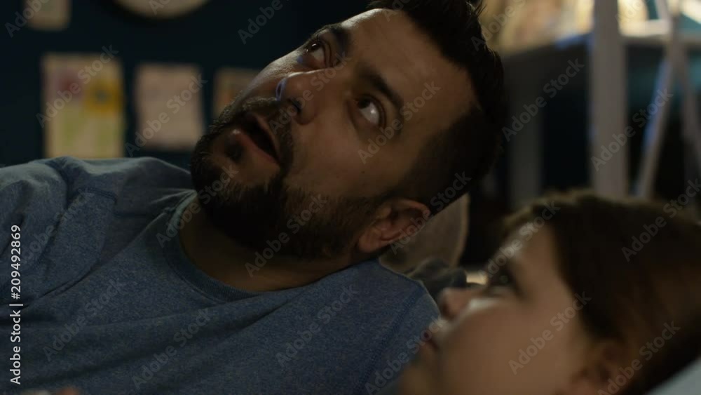 Bearded adult father lying in bed with little daughter and telling interesting story before getting to sleep Bearded adult father lying in bed with little daughter and telling interesting story before getting to sleep