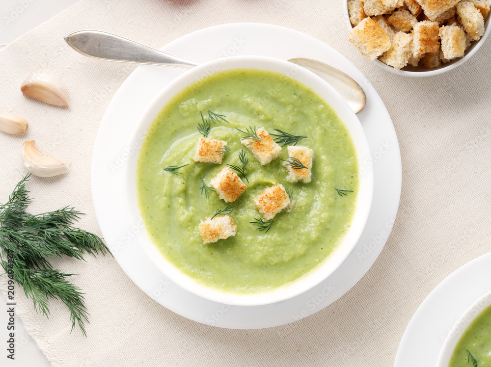 large white bowl with vegetable green cream soup of broccoli, zucchini, green peas on white background, top view large white bowl with vegetable green cream soup of broccoli, zucchini, green peas on white background, top view