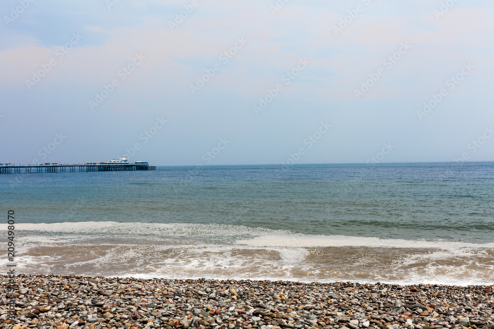 Rocky beach by the sea with waves hitting seashore. Blue sky in the background. Foam on the sea waves on the rocky beach. Nature photography with water and sky. Rocky beach by the sea with waves hitting seashore. Blue sky in the background. Foam on the sea waves on the rocky beach. Nature photography with water and sky.
