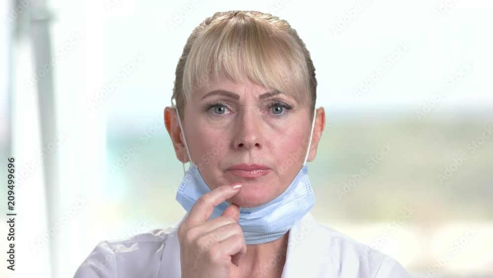 Close up female doctor is thinking. Mature woman doctor wearing face mask looking thoughtful on blurred background. Face of worried doctor.