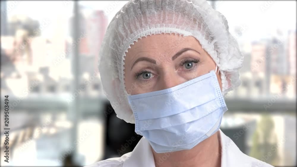 Face of female doctor in surgical cap. Woman doctor in cap and face mask putting on white protective glove close up. Face of female doctor in surgical cap. Woman doctor in cap and face mask putting on white protective glove close up.