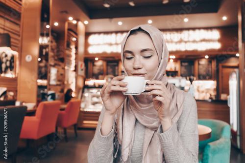 beautiful Muslim girl with a headscarf on her head drinking fragrant tea in a cozy restaurant