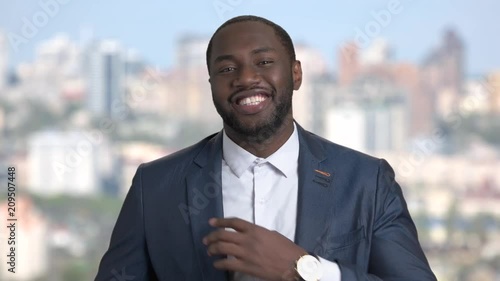 Smiling macho-man adjusting his suit. Cheerful african-american businessman adjusting his clothes on blurred background.