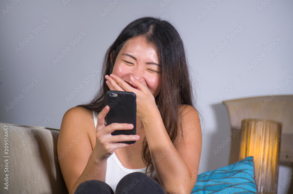 sweet happy and pretty Asian Chinese woman using internet social media app on mobile phone laughing cheerful having fun at home sofa couch sweet happy and pretty Asian Chinese woman using internet social media app on mobile phone laughing cheerful having fun at home sofa couch