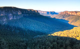 The sun casts large blue-tinted shadows on the valley floor of the Blue Mountains National Park, Australia.