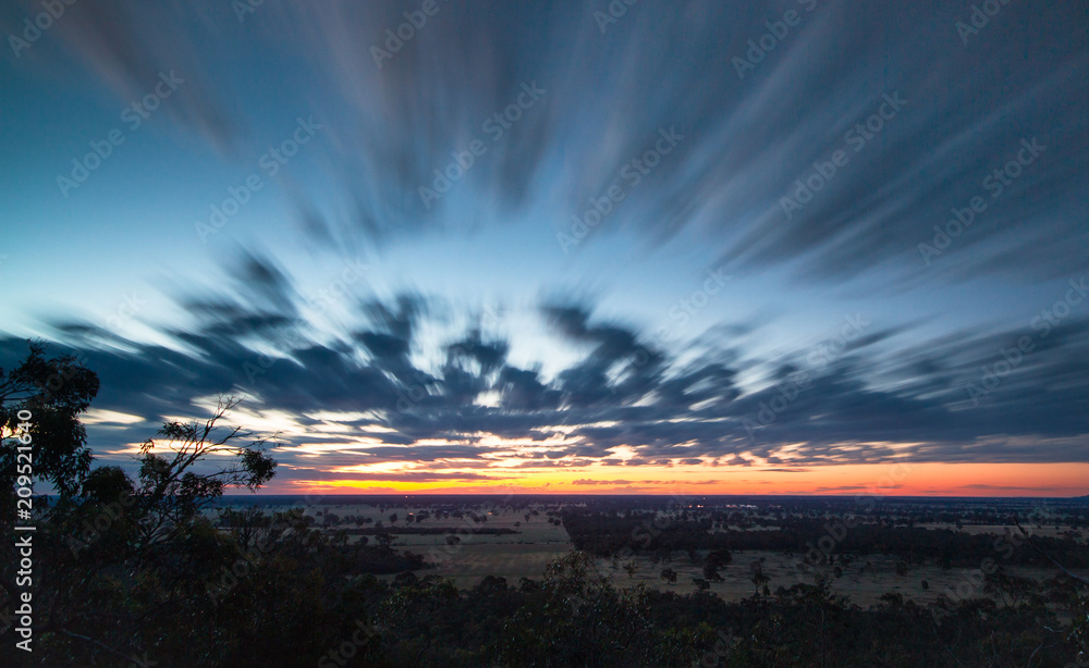 Long exposure of clouds moving across the landscape during sunset at the Black Ians Rocks near Grampians National Park, Australia. - obrazy, fototapety, plakaty 