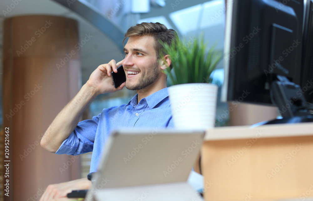 Smiling businessman sitting and using mobile phone in office. Smiling businessman sitting and using mobile phone in office.