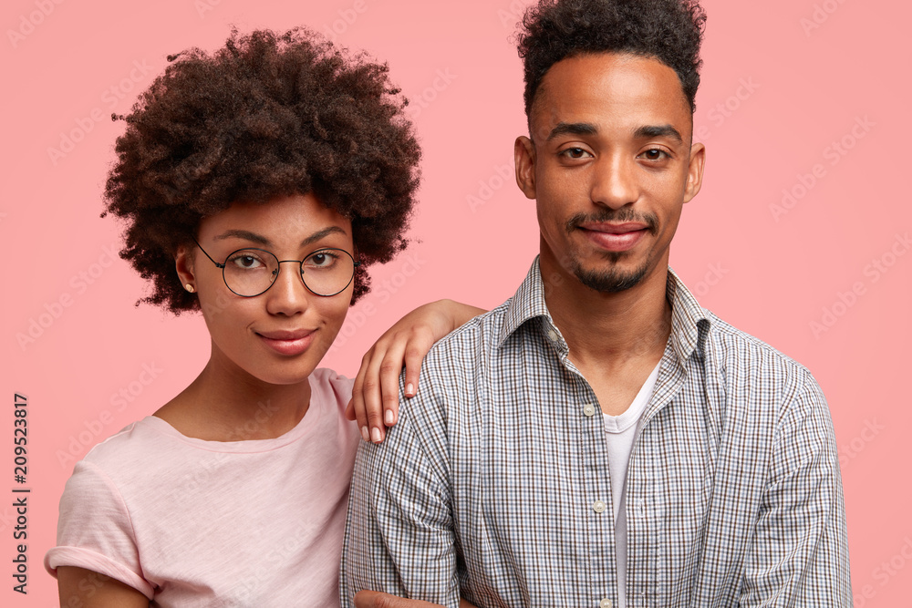 Cropped shot of friendly woman and man companions stand close to each other, look seriously and confidently at camera, listen important information, isolated on pink studio wall, dressed casually Cropped shot of friendly woman and man companions stand close to each other, look seriously and confidently at camera, listen important information, isolated on pink studio wall, dressed casually