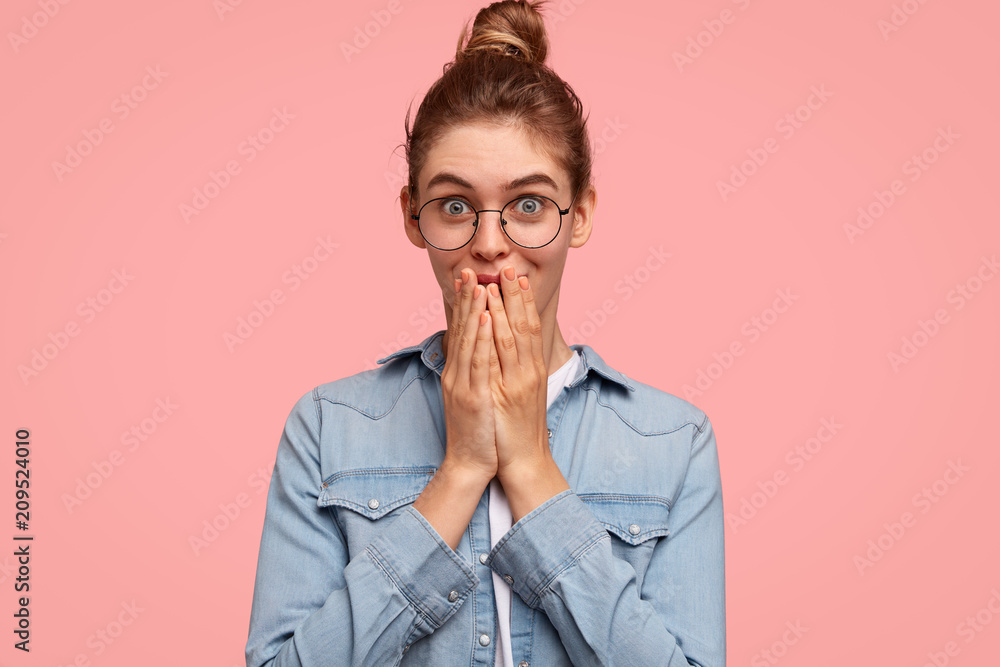 Indoor shot of pretty pleased female tries to stop giggling, looks joyfully at camera, gossips with friend, discuss colleagues and their personal life, wonders some news, has dark hair tied in bun Indoor shot of pretty pleased female tries to stop giggling, looks joyfully at camera, gossips with friend, discuss colleagues and their personal life, wonders some news, has dark hair tied in bun