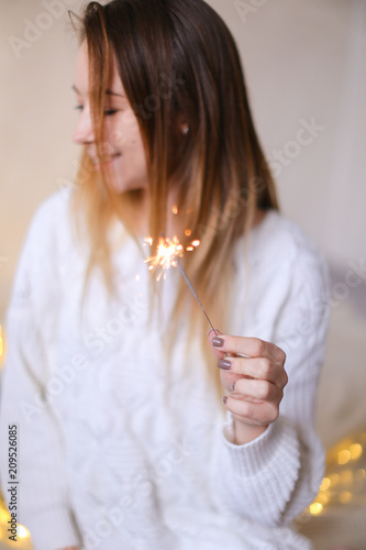 Young blonde woman sitting with bengal light near twinkling yellow garlands. Concept of positive emotions and celebration New Year holidays. photo