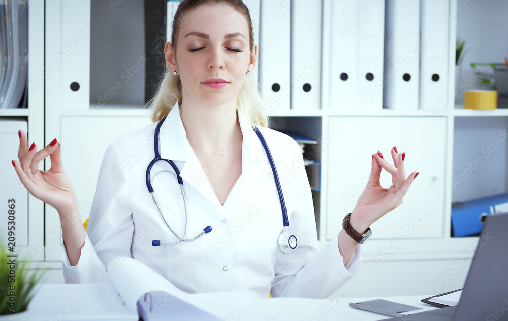 Young blonde female medical doctor doing yoga and relaxing with eyes closed at workplace. Short break in the hard work. Young blonde female medical doctor doing yoga and relaxing with eyes closed at workplace. Short break in the hard work.