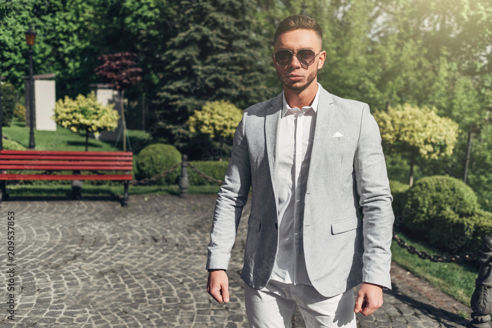 Young Guy with Beard and with Glasses in Stylish Suit Posing on the Street in the Sunlight Young Guy with Beard and with Glasses in Stylish Suit Posing on the Street in the Sunlight