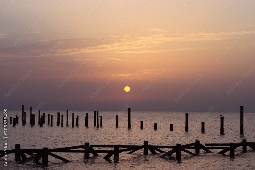Obraz premium Sunrise on the sea. Wooden piles of destroyed pier sticking out of the water. Morning sun rays. Red sea, Safaga, Egypt.