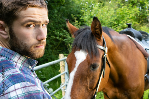 Handsome American cowboy, rider with checked, chequered shirt and jeans pets and loves his horse