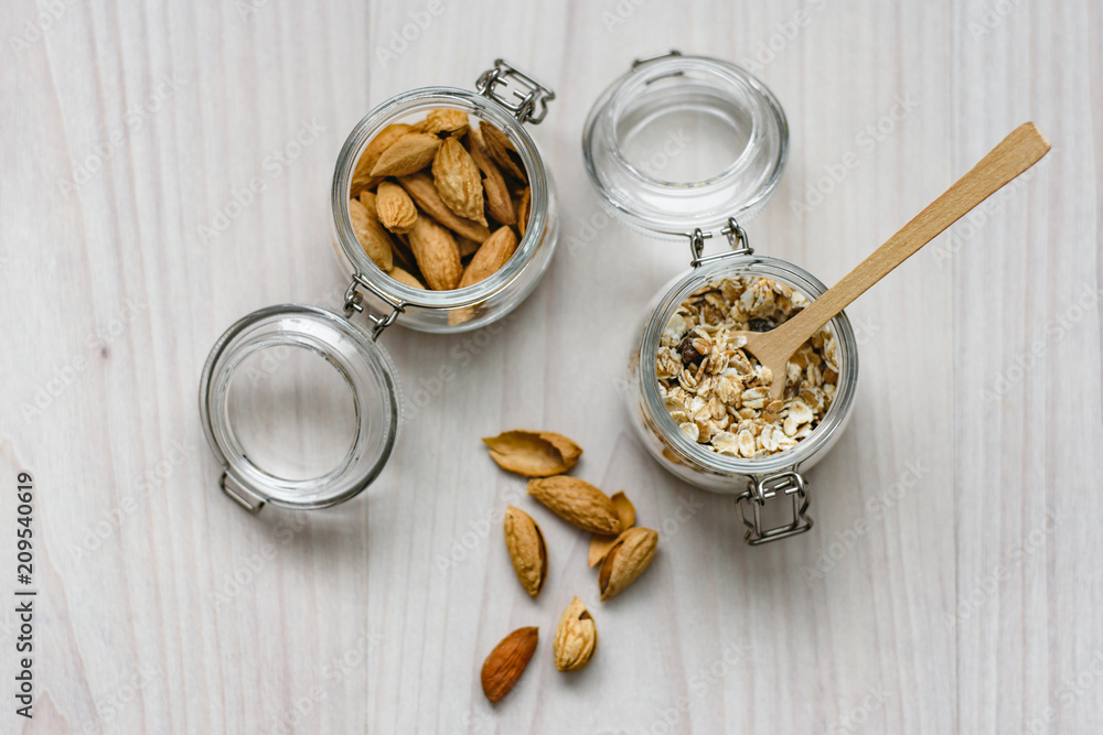 Fototapeta premium Still life of healthy food and diet food, almonds, wooden spoon and muesli in glass jars on a wooden background.