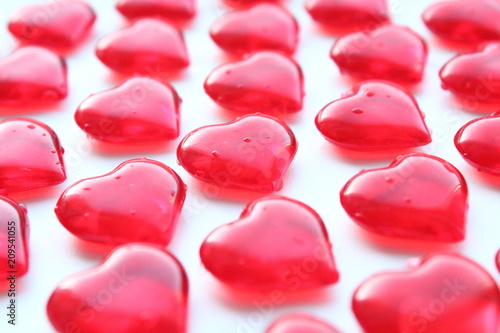 Beautiful decorative volumetric red hearts made of glass scattered on a white surface. Close-up. Background. Texture.