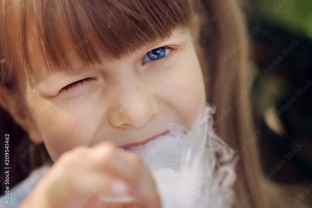 A beautiful naughty little blue-eyed light-blue girl walks in a sunny summer park and eats sweet cotton candy A beautiful naughty little blue-eyed light-blue girl walks in a sunny summer park and eats sweet cotton candy