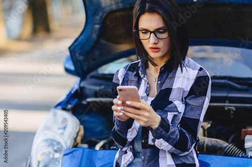 attractive girl with phone near open hood of car