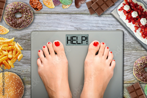 Junk food or sugar sweets temptations when you diet concept with woman feet on weight scale
