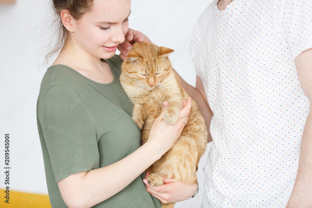 Attractive cute couple is holding his domestic ginger cat in arms. Young beautiful family loves her pet. People and animal Attractive cute couple is holding his domestic ginger cat in arms. Young beautiful family loves her pet. People and animal