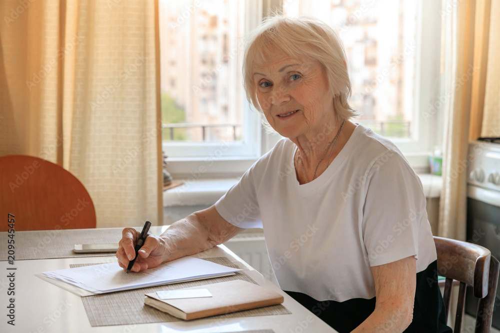 Elderly woman plans her budget, with a notebook, bills and a credit card. Increase in retirement age, savings for a retirement Elderly woman plans her budget, with a notebook, bills and a credit card. Increase in retirement age, savings for a retirement