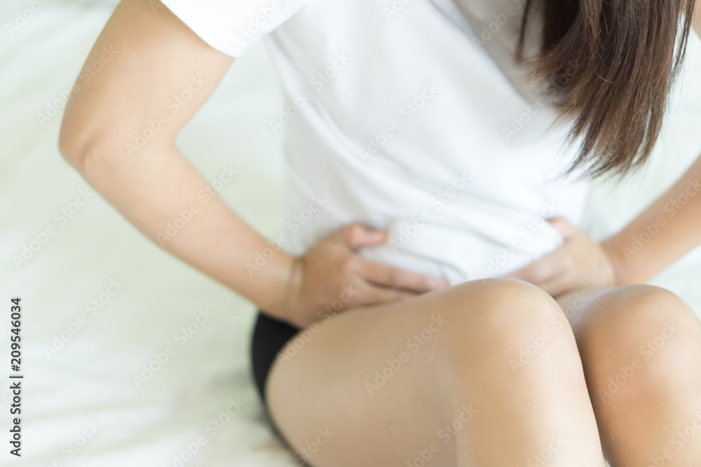 Closeup woman hand holding abdominal with stomach ache lying on bed, health care and medical concept Closeup woman hand holding abdominal with stomach ache lying on bed, health care and medical concept