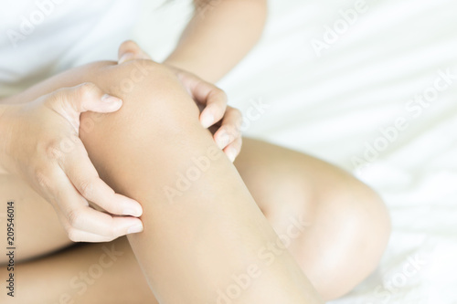 Closeup woman hand holding knee with pain on bed, health care and medical concept