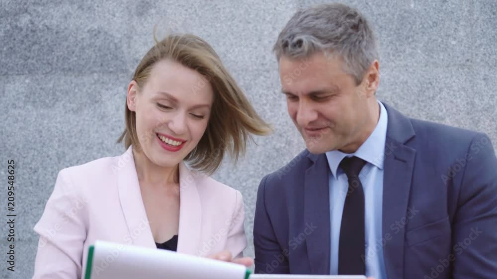 Business man and woman businesspeople sitting on the railing near the office building and discussing the project. A man and a middle-aged woman. people are holding documents and a tablet 4k Business man and woman businesspeople sitting on the railing near the office building and discussing the project. A man and a middle-aged woman. people are holding documents and a tablet 4k