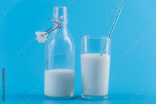 Bottle of fresh milk and a glass with a straw on a blue background. Concept of healthy dairy products with calcium