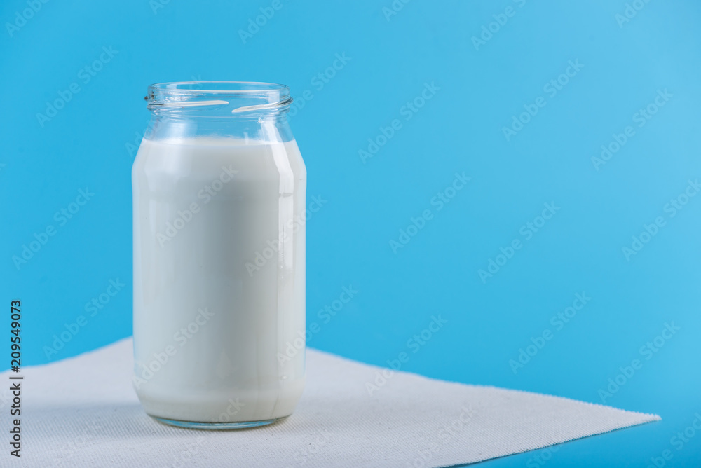 Glass bottle with fresh milk on blue background. Colorful minimalism. Healthy dairy products with calcium Glass bottle with fresh milk on blue background. Colorful minimalism. Healthy dairy products with calcium