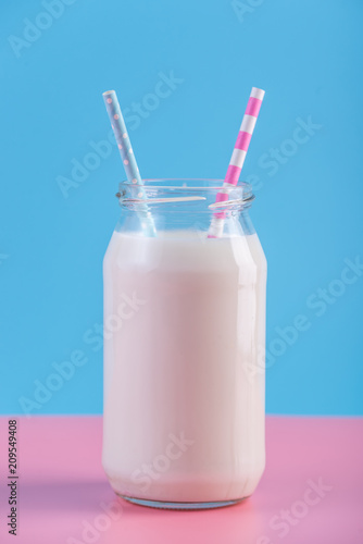 Bottle of fresh milk with two straws on pastel background. Colorful minimalism. Healthy dairy products with calcium