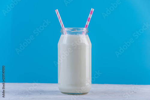 Glass bottle of fresh milk with two straws on blue background. Colorful minimalism. Healthy dairy products