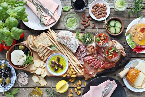       Mediterranean appetizers table concept. Dinner table with tapas selection  cured meat and salami  gazpacho soup  jamon  olives  cheese  hummus and vegetables. Overhead view.