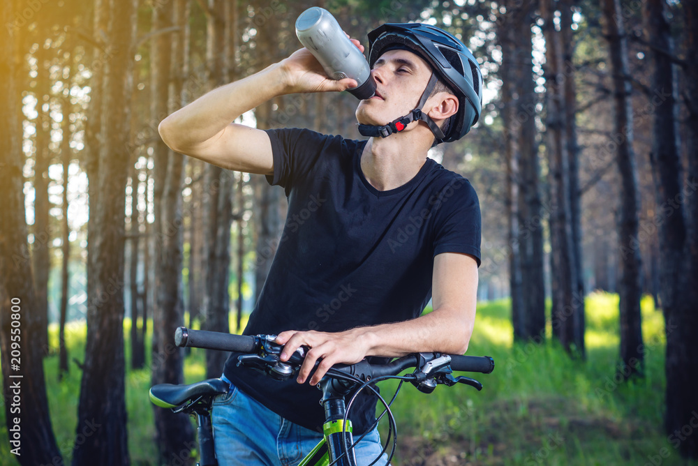 Obraz premium Cyclist in a helmet drinking water from a bottle while riding in the Park. Concept of active and healthy lifestyle