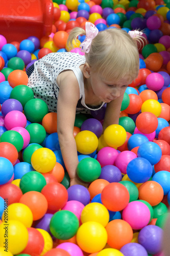 A girl in the playroom, where there are a lot of colored balls.