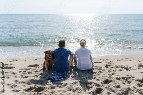 Mom with her son and their dog sitting on the beach watching the sunset